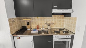 Uma cozinha compacta com fogão, pia e um forno pequeno. Há utensílios e um escorredor de louça.