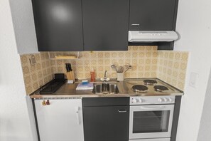 Eine kompakte Küche mit Herd, Spüle und kleinem Backofen. Es befinden sich Geschirr und ein Abtropfgestell dort.