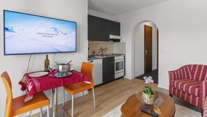 Uma sala de estar moderna com área de jantar, cozinha e uma TV exibindo uma paisagem montanhosa nevada.