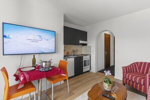 Ein modernes Wohnzimmer mit Essbereich, Küche und einem Fernseher, der eine verschneite Berglandschaft zeigt.