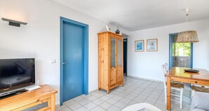 A room with a television, a wooden cabinet, a dining table with chairs, and a blue door. - Sea-view apartment in El Golfet (Calella de Palafrugell)