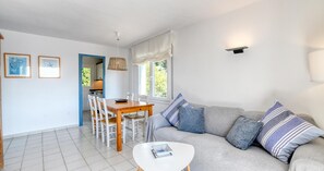 A modern living room with a grey sofa, a white coffee table, and a dining area with a wooden table and white chairs. - Sea-view apartment in El Golfet (Calella de Palafrugell)
