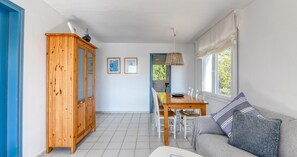 A room with a wooden cabinet, a dining table with chairs, a sofa with cushions, and a window with curtains. - Sea-view apartment in El Golfet (Calella de Palafrugell)
