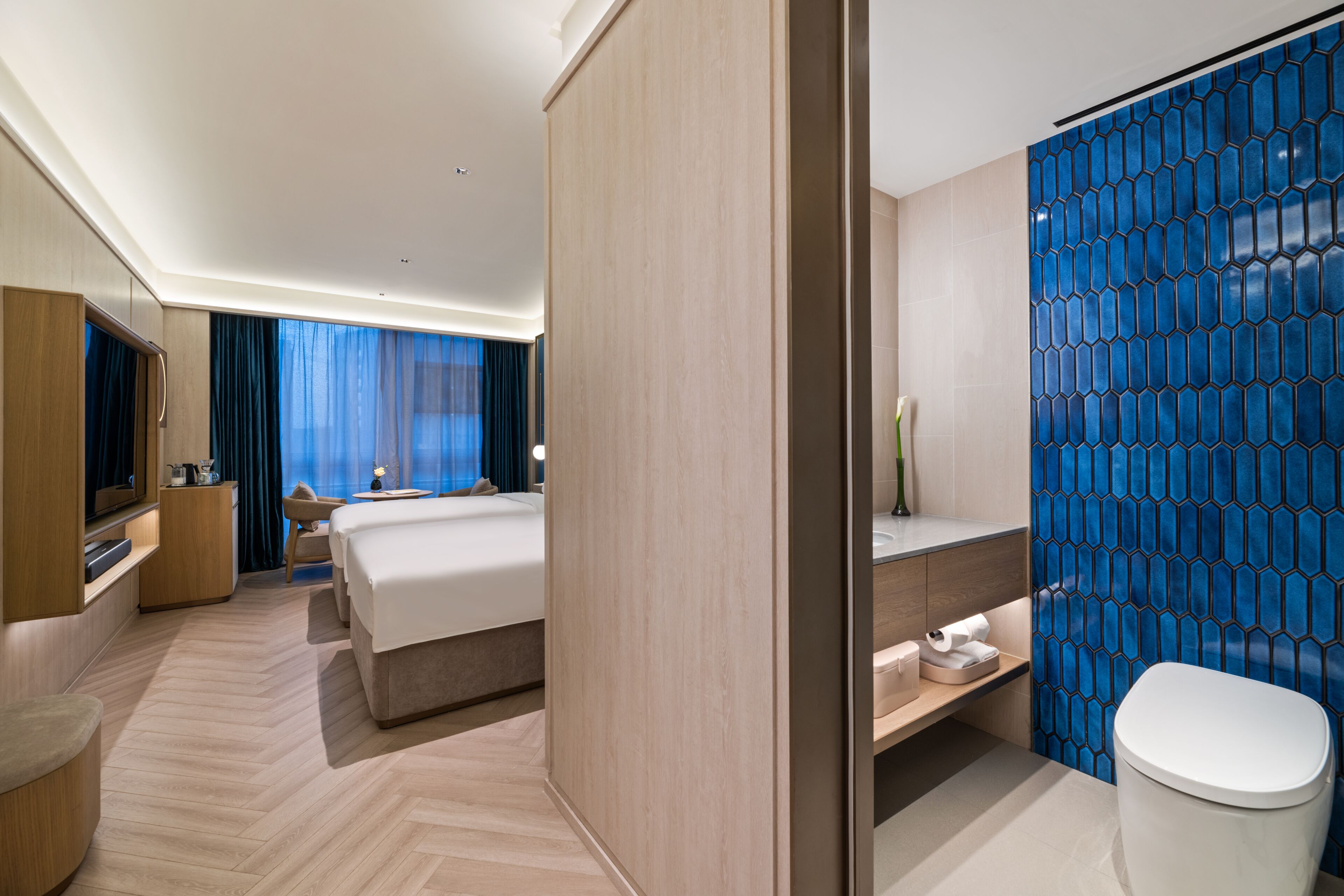 Una habitación de hotel moderna con una cama, mesita de noche, televisión y un baño con inodoro y lavabo.