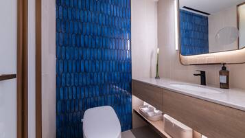 A modern bathroom with a blue hexagonal tile wall, a white toilet, a vanity with a mirror, and a sink.