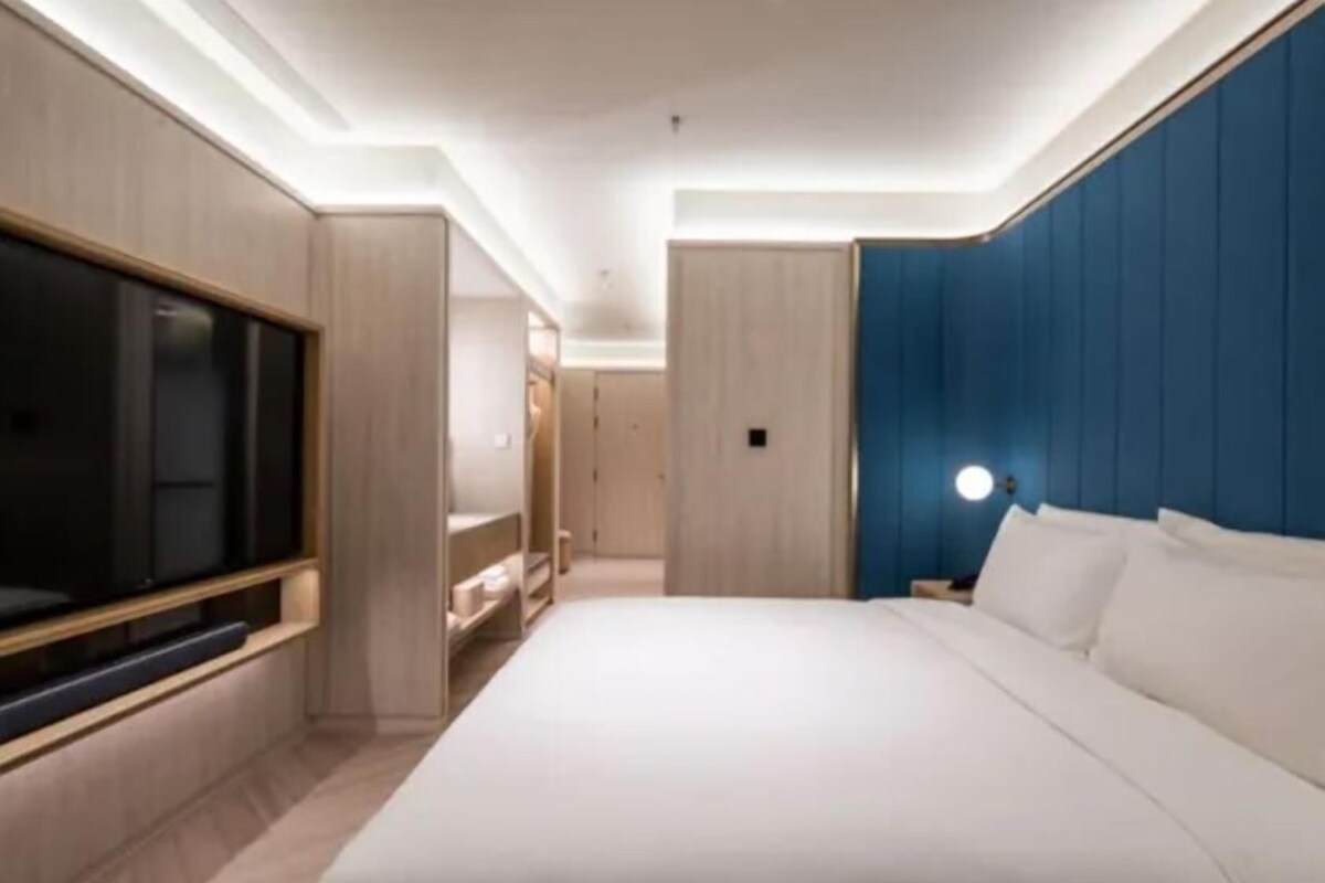 A modern hotel room with a large bed, a TV mounted on the wall, and a blue accent wall.