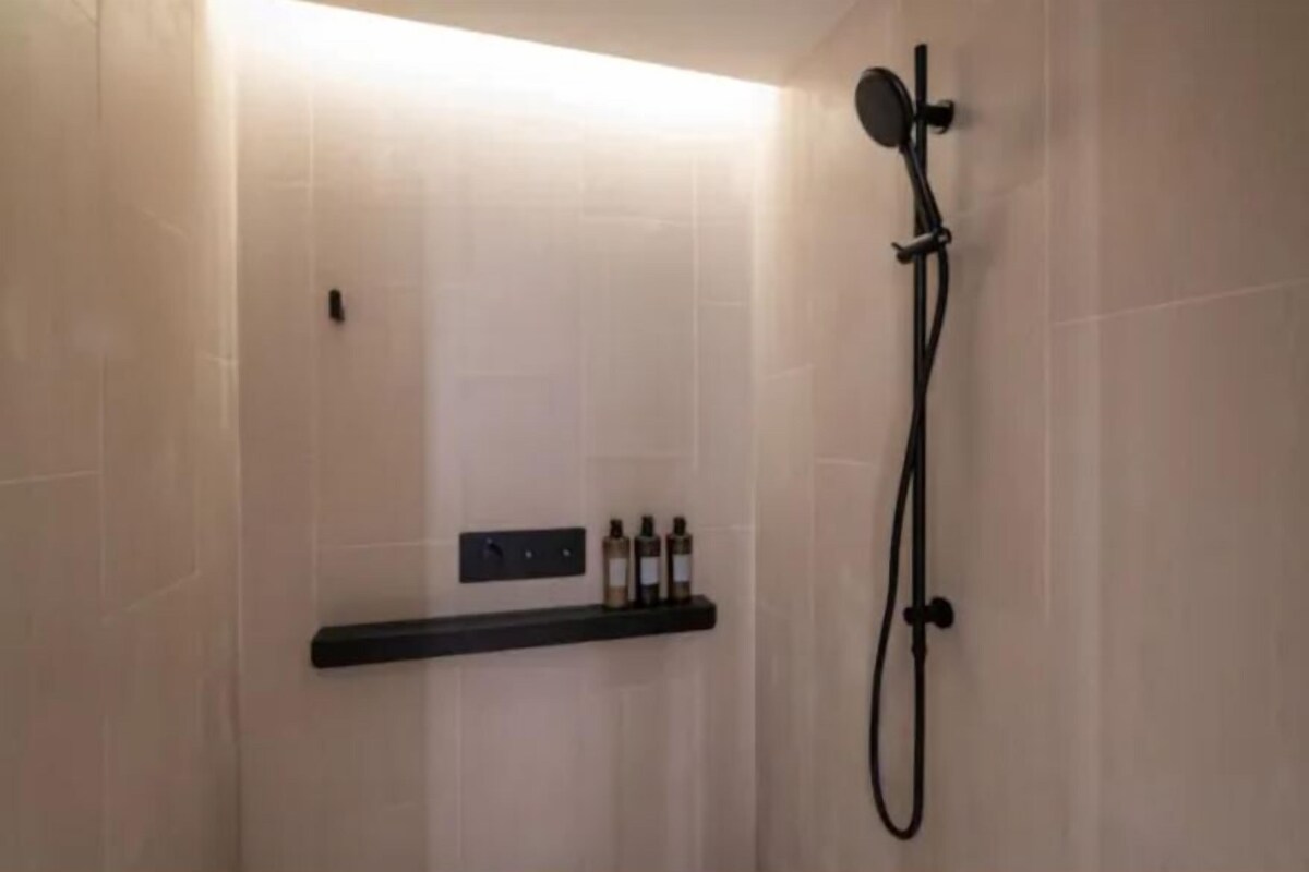 A modern shower area with a handheld showerhead and a wall-mounted control panel.