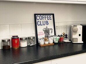 A kitchen counter with a coffee machine, various containers of coffee and sugar, and a framed sign that reads 'COFFEE CLUB Every Morning.' - Walk to Everything | Sleeps 4 | 2 Bed | Bold St (Merseyside)