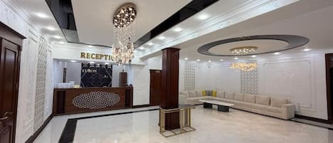 A reception area with a reception desk, a chandelier, a sofa, and a patterned wall.