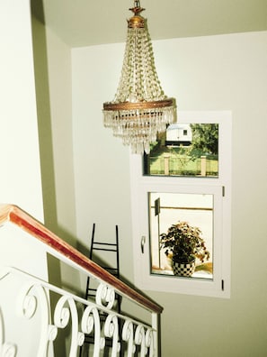 A staircase with a white railing, a chandelier, and a framed picture of a house. - Casa Calma | Somewhere Between Venice and Everything Else (Noale)