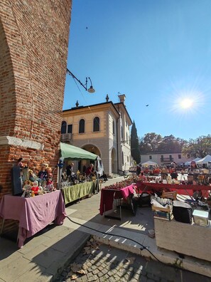 An outdoor market with tables displaying various items, a brick building, and a clear blue sky. - Casa Calma | Somewhere Between Venice and Everything Else (Noale)