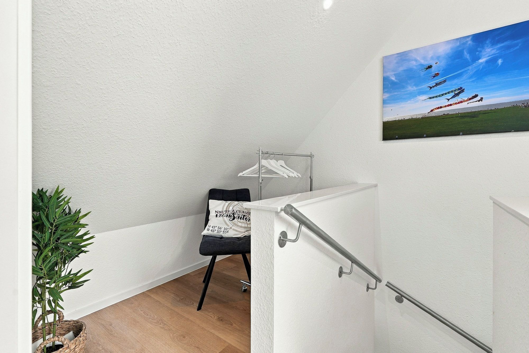 Een trap met een leuning, een aan de muur hangend schilderij, een kledingrek en een pot met een plant.