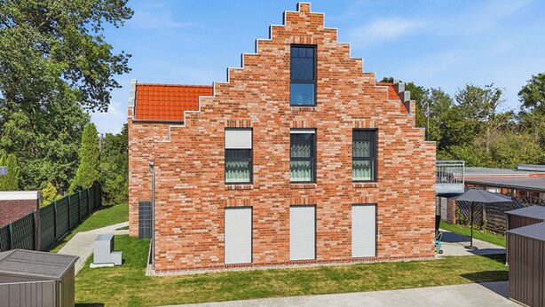 Ein Backsteinhaus mit einer gestuften Dachkonstruktion, zahlreichen Fenstern und einer Garagenöffnung.