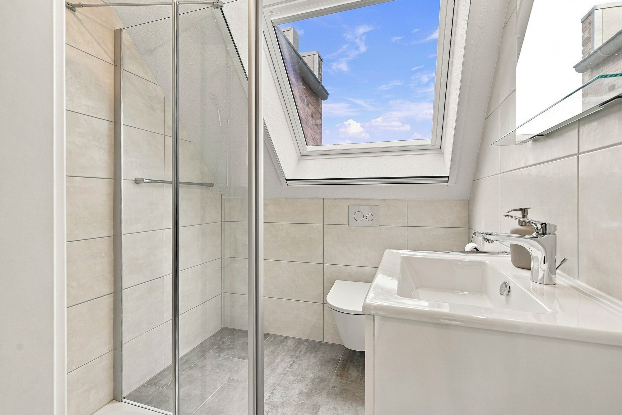 A modern bathroom with a glass shower enclosure, a skylight, and a white sink.