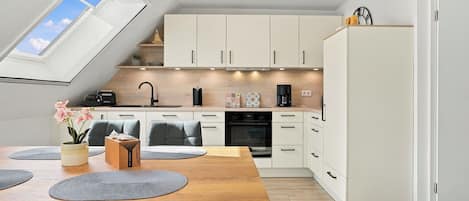 A modern kitchen with white cabinets, a wooden dining table, and a skylight.
