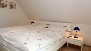 Ein Schlafzimmer mit einem Bett, einem Nachttisch, einer Lampe und zwei gerahmten Bildern an der Wand.