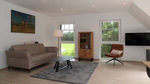 A living room with a sofa, a coffee table, a bookshelf, a chair, and a TV.