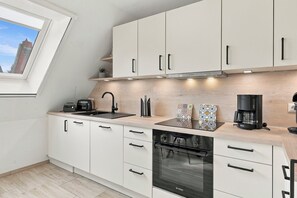 Eine moderne Küche mit weißen Schränken, einem Backofen von Bosch, einer Kaffeemaschine und einem Fenster mit Blick auf ein Gebäude.