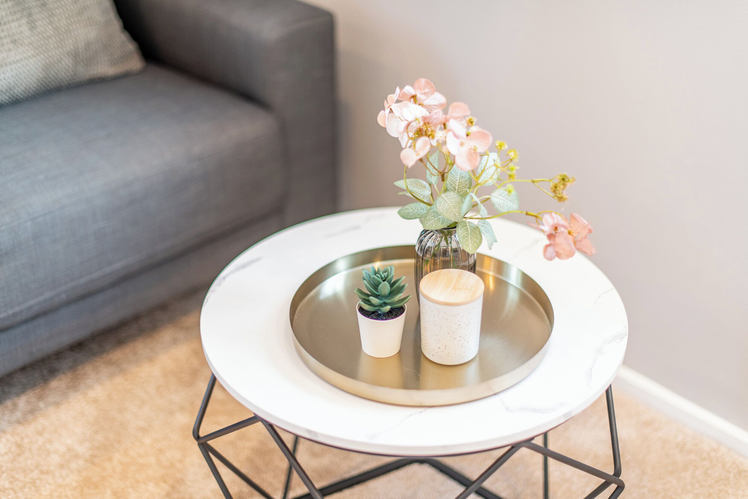 A round table with a white marble top, a small potted succulent, and a vase with pink flowers.