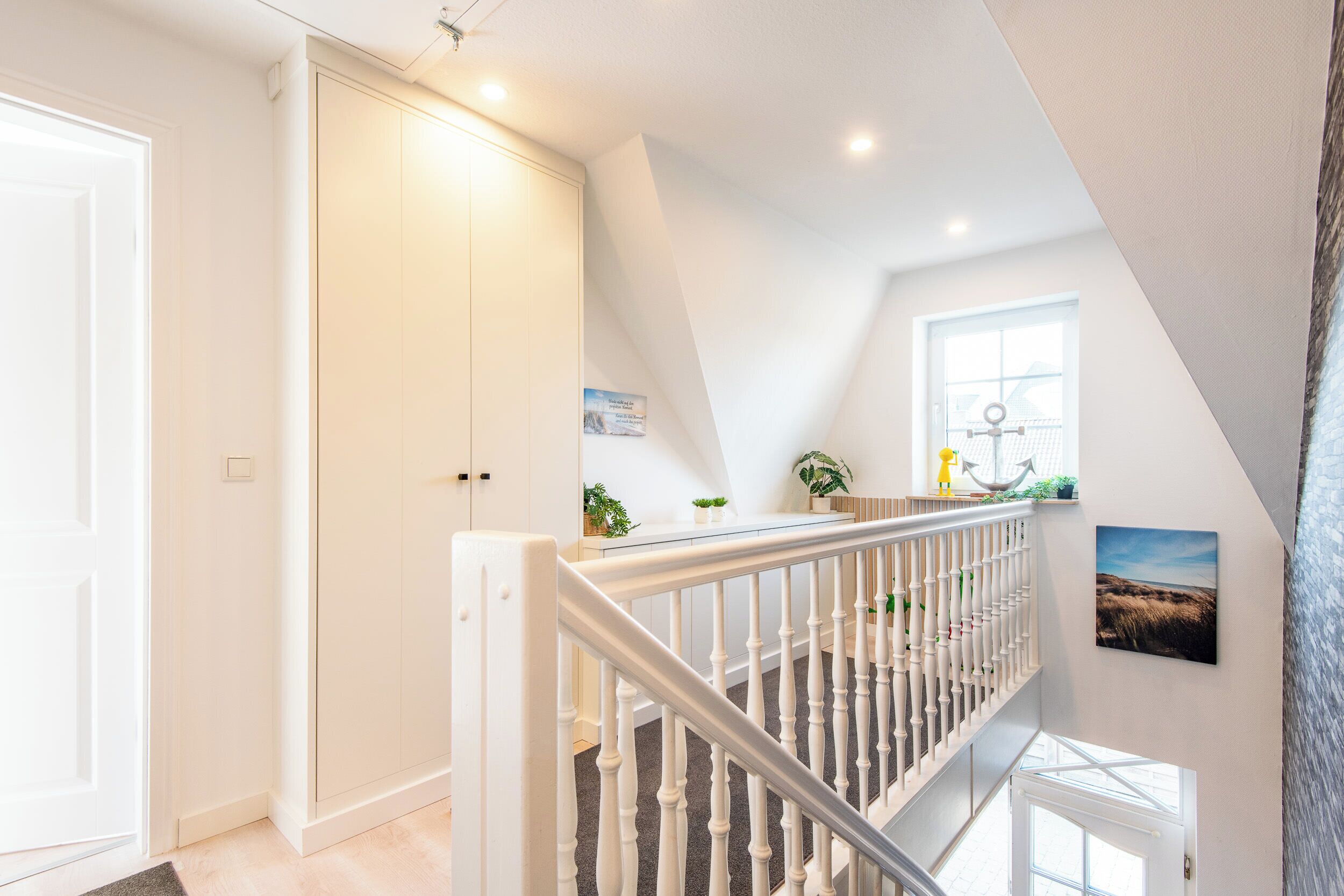 A staircase with white balusters leading to an upper floor, a door with a light switch, and a window with a view of the sky.