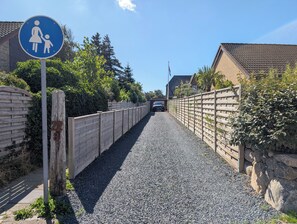 A residential street with a blue pedestrian sign, a gravel driveway, wooden fences, and houses with tiled roofs. - Vacation Home "Westerlön Hüs 1999" (Sylt)