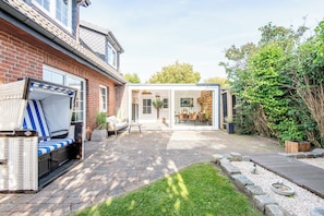A patio with a wicker sofa, a glass-enclosed dining area, and a brick house. - Vacation Home "Westerlön Hüs 1999" (Sylt)