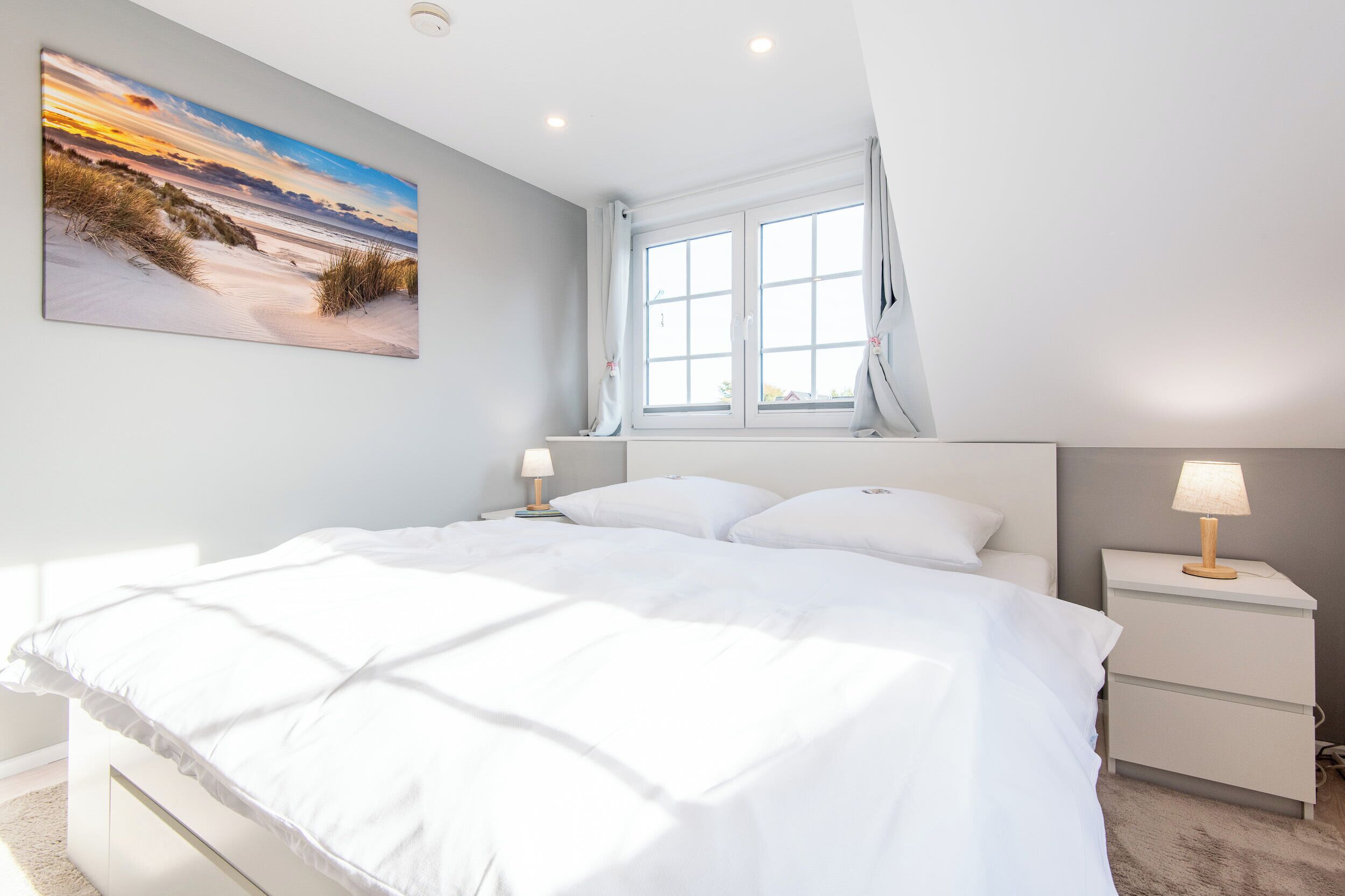 Een slaapkamer met een groot bed, een nachtkastje, een lamp en een raam met gordijnen.