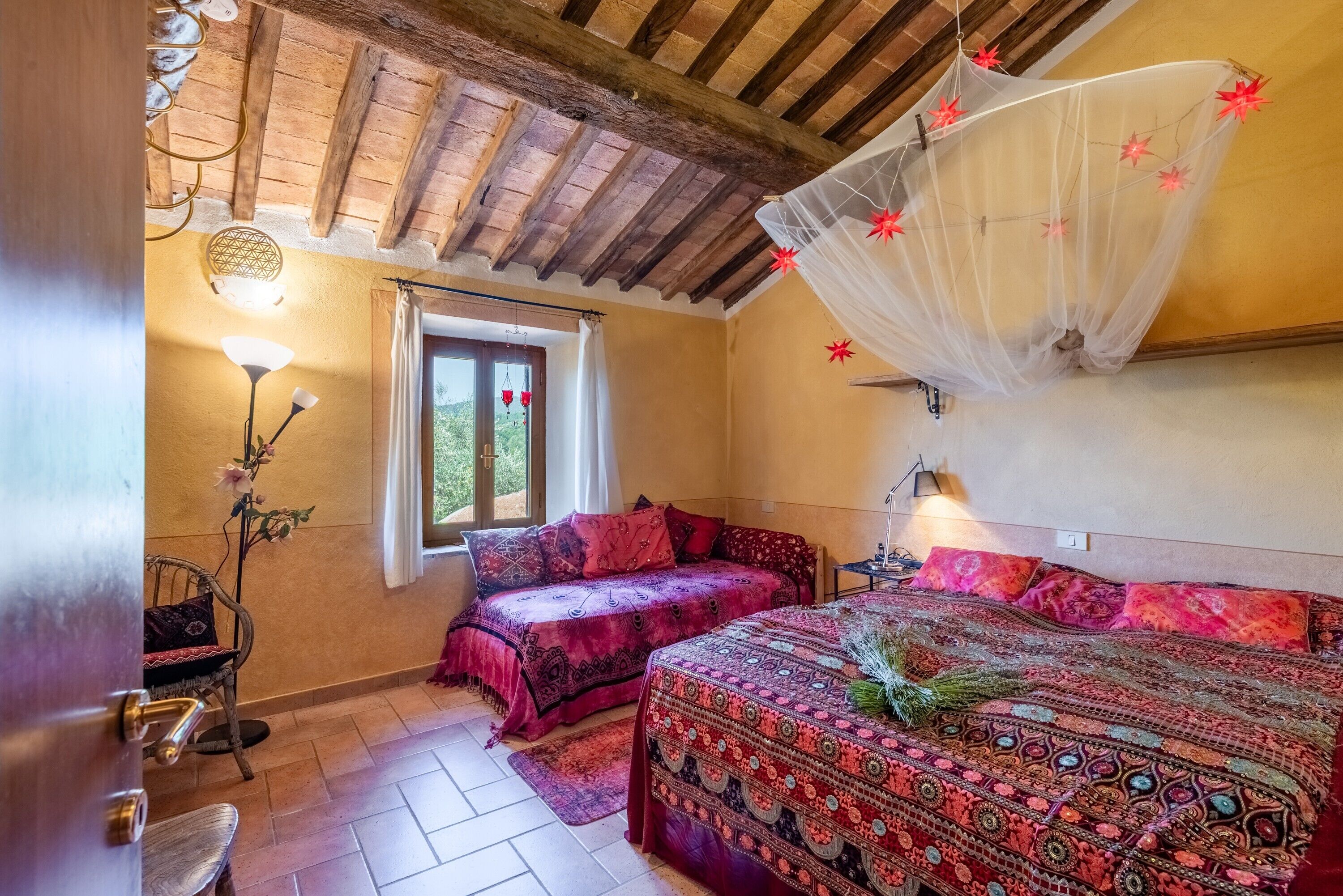 Un dormitorio acogedor con dos camas, techo de madera, ventana con cortinas y mosquitero colgado.
