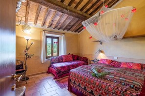 A cozy bedroom with two beds, a wooden ceiling, a window with curtains, and a hanging mosquito net.