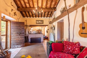 A rustic interior with exposed wooden beams, a chandelier, a guitar, and a cozy seating area.