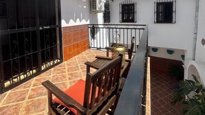 Eine Terrasse mit einer hölzernen Bank, einem Fliesenboden und einem weißen Gebäude mit schwarzen Fensterläden.