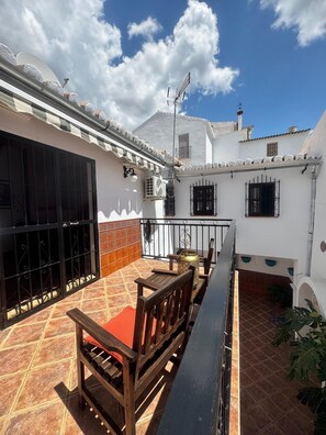 A patio with a wooden bench, a tiled floor, and a white building with black window bars. - The Courtyard of the Soul (villanueva de la concepción)