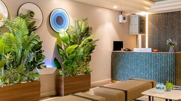 A modern hotel lobby with seating areas, a reception desk, and decorative plants.