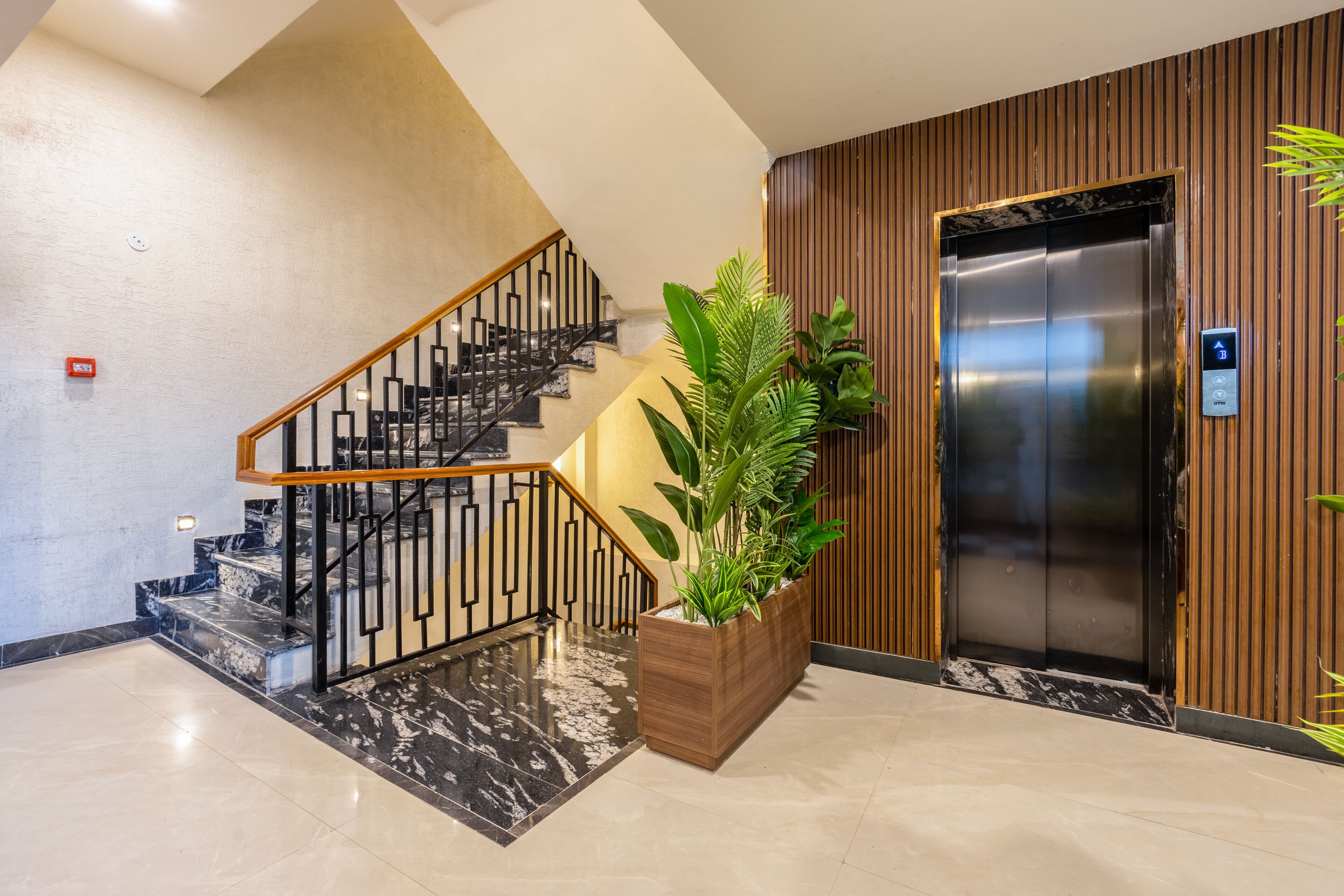 Un interior moderno con una escalera de mármol, un panel de madera y una planta grande en maceta.