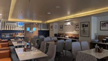 Un comedor de hotel con varias mesas y sillas, una cocina al fondo y cuadros en las paredes.