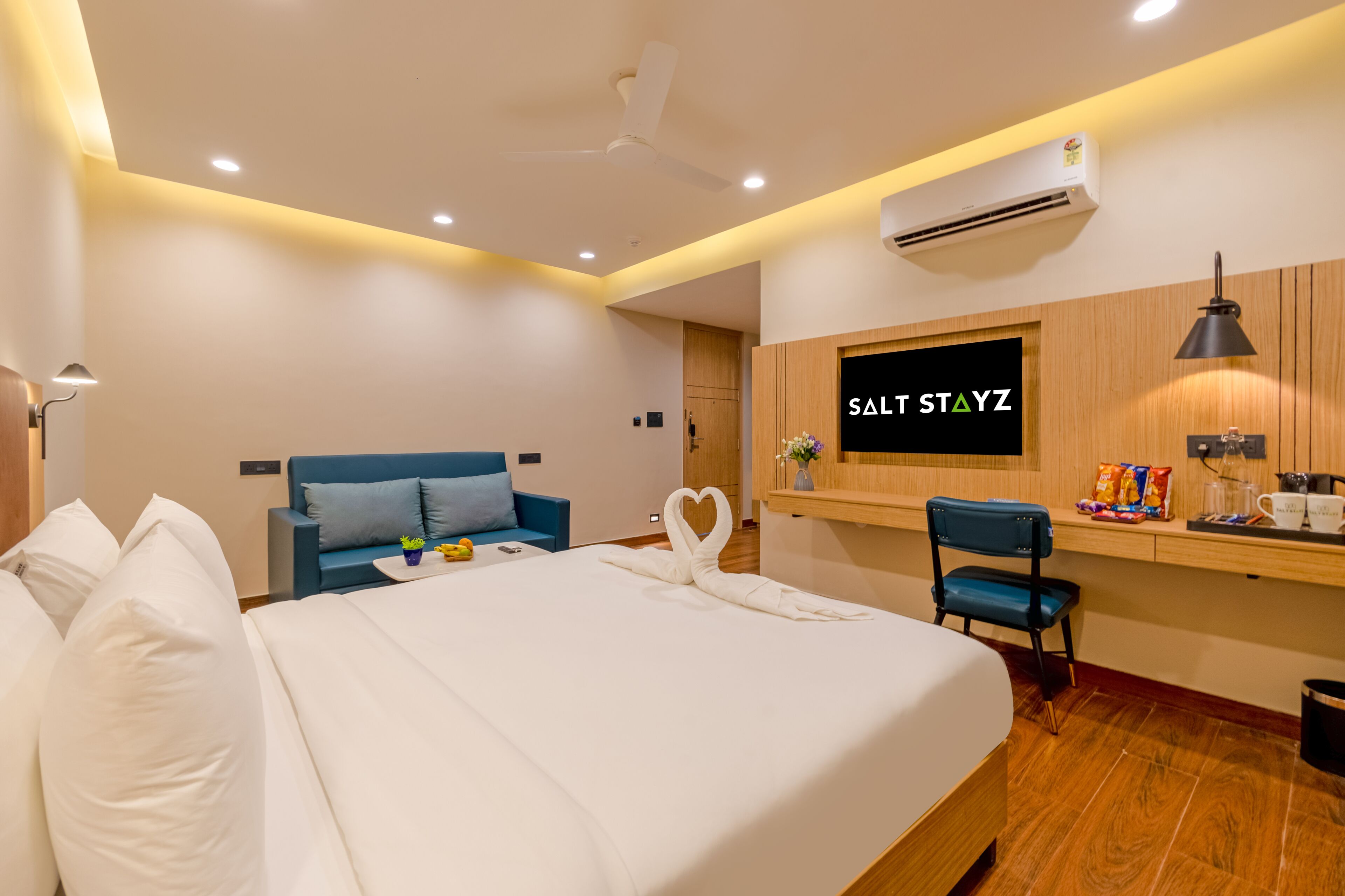 A hotel room with a bed, a desk, a chair, a TV, and an air conditioning unit.