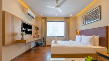 Habitación de hotel con cama, televisor montado en la pared, ventilador de techo y ventana con cortinas.