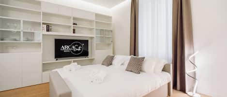 A modern hotel room with a bed, a TV mounted on a white wall, and a built-in shelf unit.