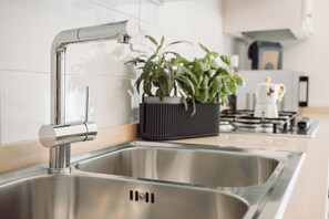 Una cocina moderna con lavamanos de acero inoxidable, una olla negra con plantas verdes y una estufa al fondo.