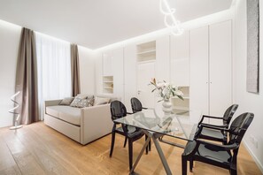 Un moderno salón con una mesa de comedor de cristal, sillas negras, un sofá y un armario blanco.