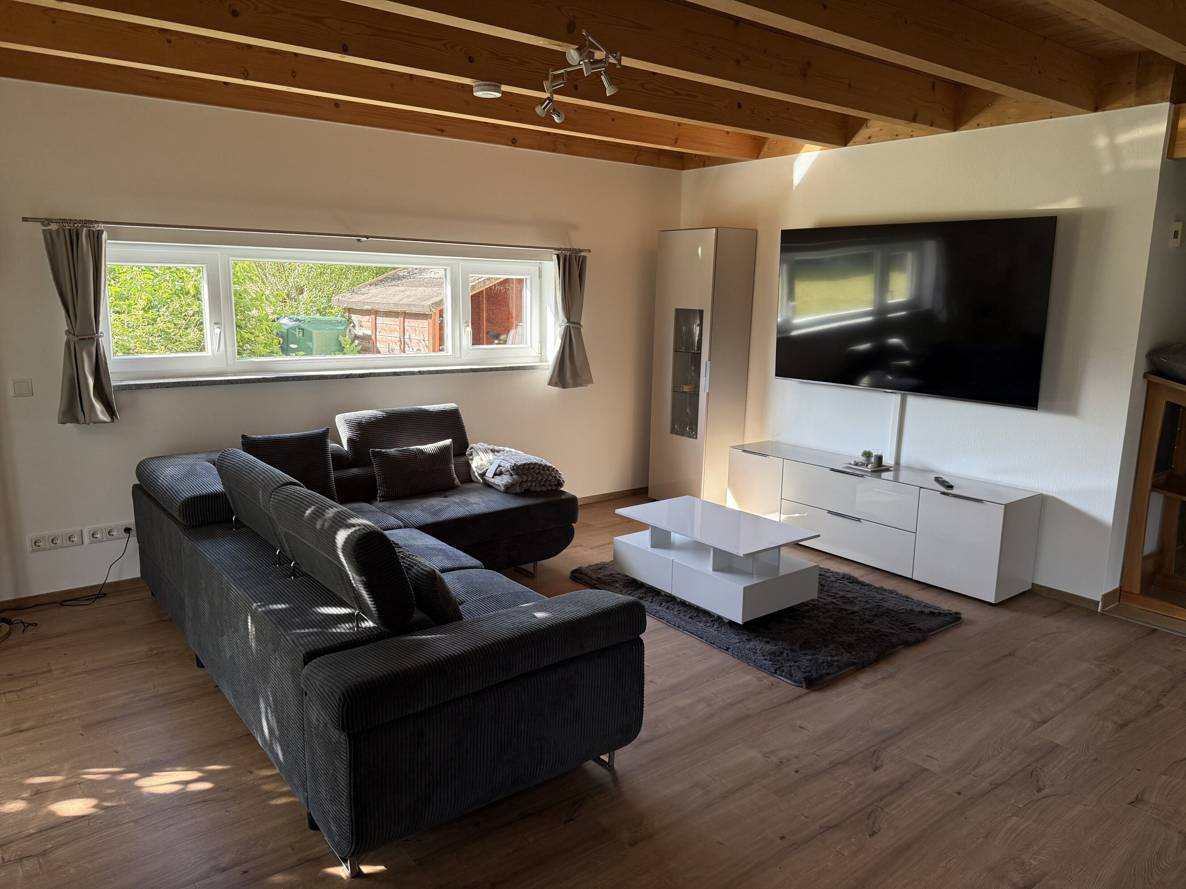 A modern living room with a sectional sofa, a white coffee table, a flat-screen TV, and a wooden ceiling.