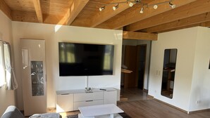 Ein modernes Wohnzimmer mit einem großen Flachbildfernseher, einer weißen Unterhaltungsecke, einem grauen Sofa und einer Holzbodenverkleidung.