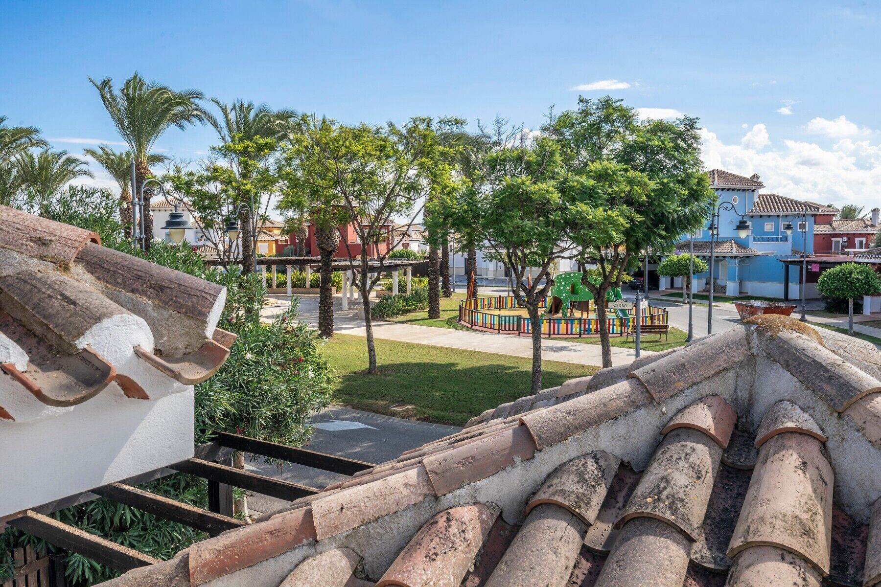 Zona residencial con un parque infantil, palmeras y edificios tradicionales.