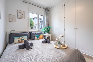 Un dormitorio con cama, almohadas, una mesita de noche con planta, una ventana y un armario.