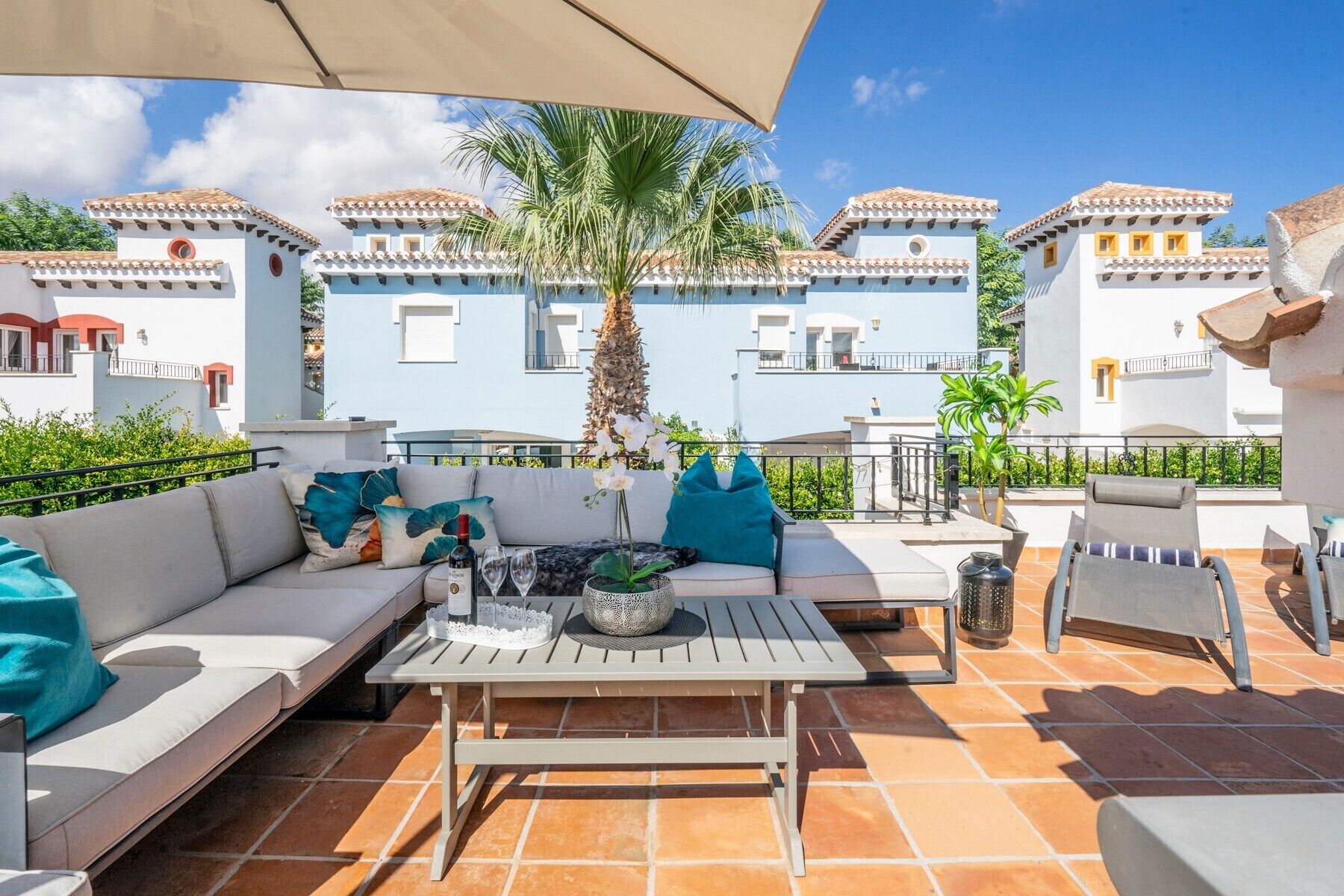 Una terraza con sofá, mesa y sillas, con vistas a un edificio azul con balcones.