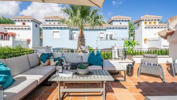 Una terraza con sofá, mesa y sillas, con vistas a un edificio azul con balcones.