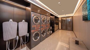A modern laundry facility with multiple washing machines and dryers, a seating area, and a glass door leading to another room.