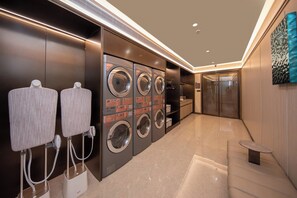 A modern laundry facility with multiple washing machines and dryers, a seating area, and a glass door leading to another room.