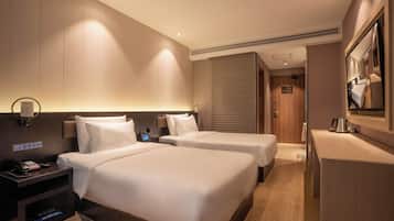 A hotel room with two beds, a desk, a mirror, a phone, and a control panel on the wall.