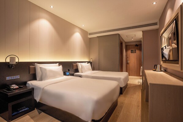 A hotel room with two beds, a desk, a mirror, a phone, and a control panel on the wall.